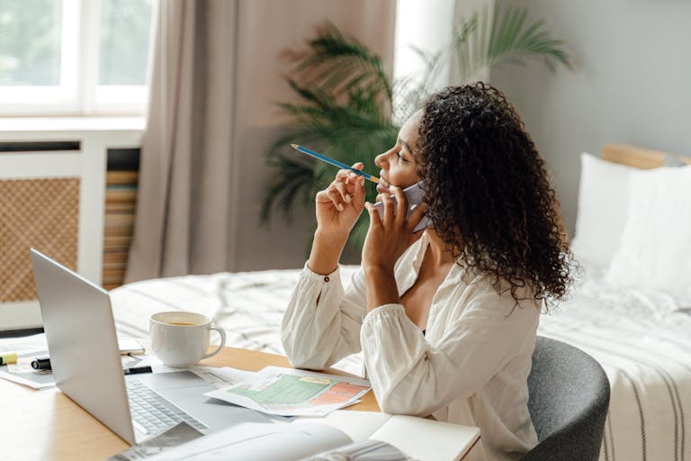 Woman multitasking with phone and laptop in a cozy home office setting.